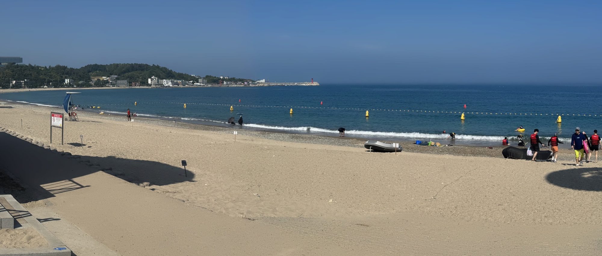관성솔밭해변 전경 — 백사장과 부표 라인, 멀리 방파제와 빨간 등대
